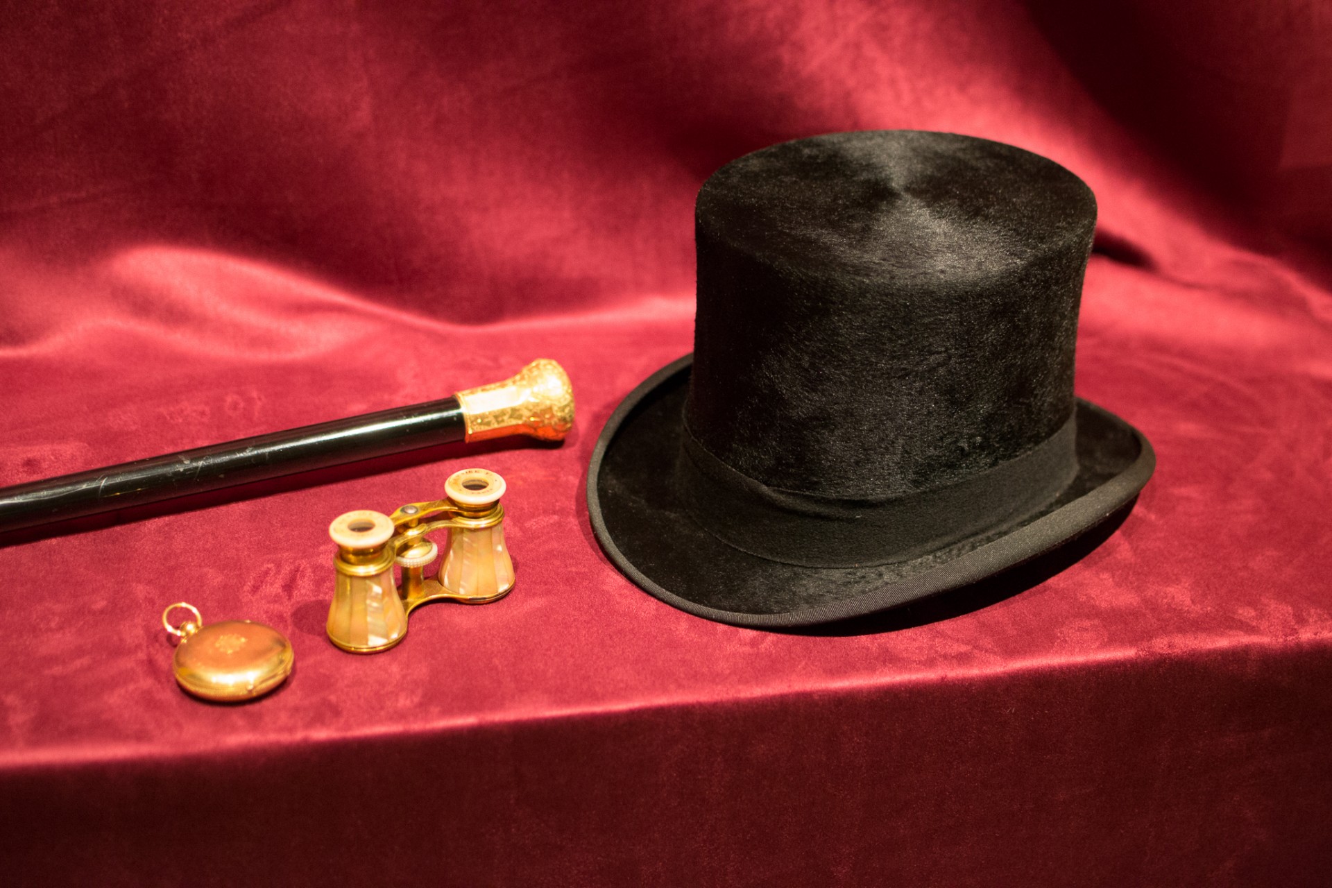 Top hat, binoculars, a stopwatch, and a cane on red velvet.