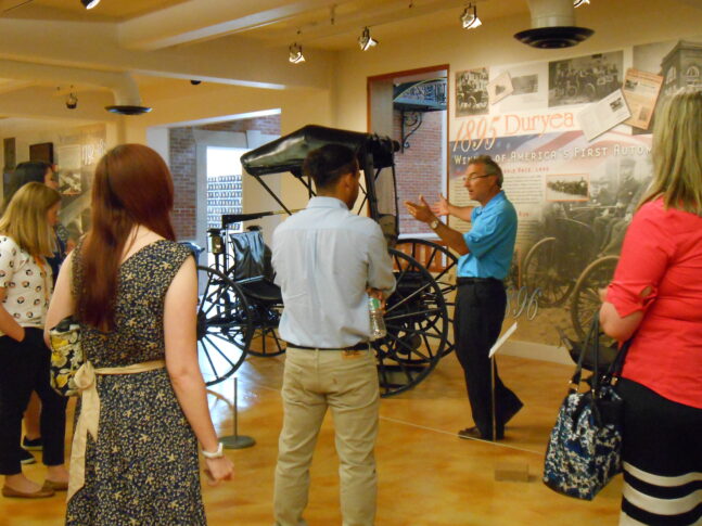 Docent guide discusses antique automobile with students