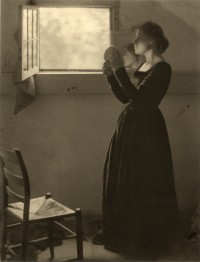 Photo of woman standing next to a window holding a mirror