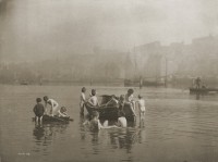 Black and white photo of boys around a boat in shallow water.