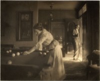 Black and white image of a woman playing billiards at left with a man with billiard cue looking out the door.