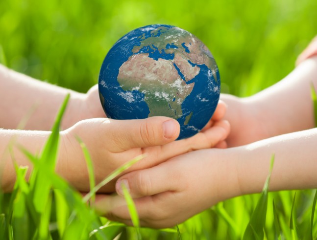 Earth in children`s hands against green spring background