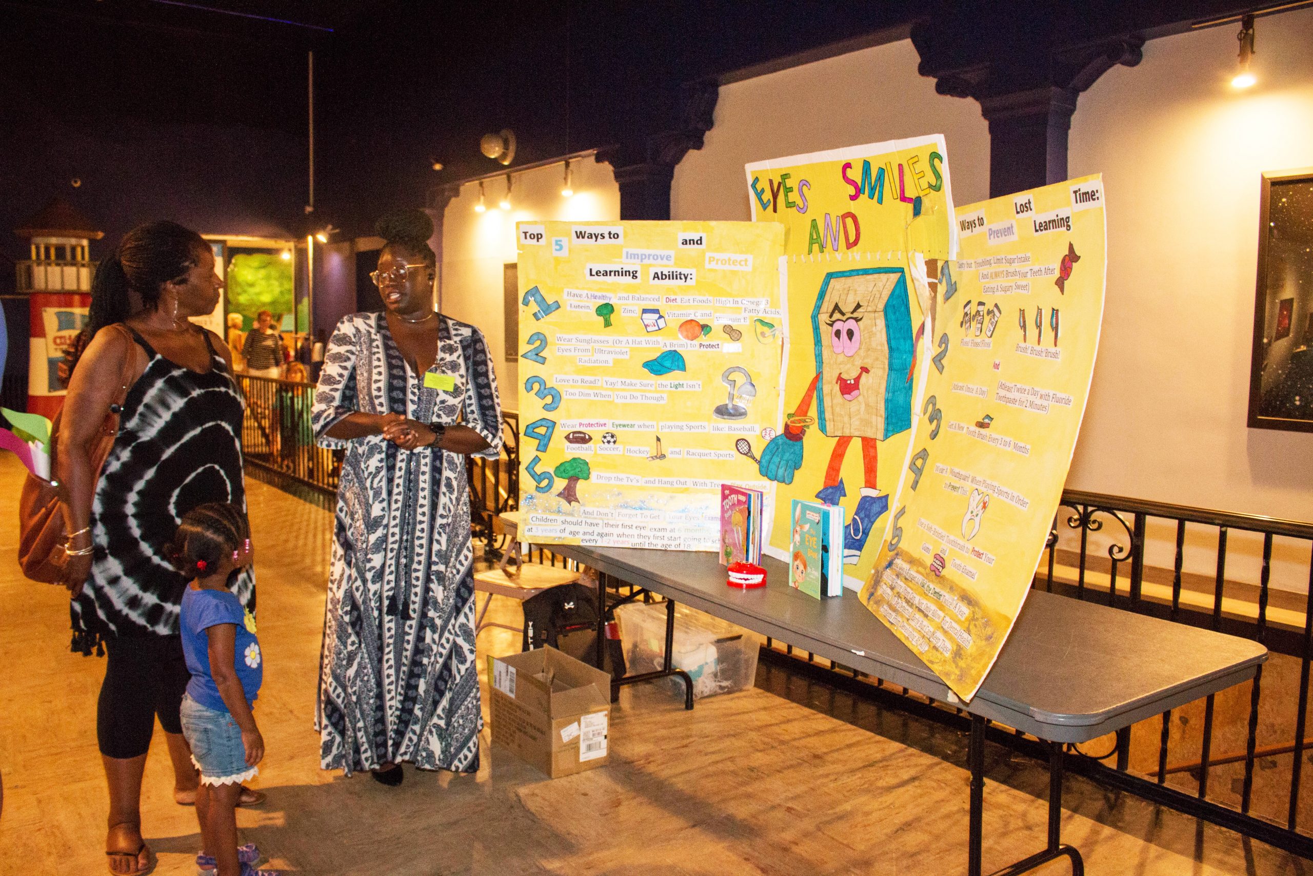 A woman and a girl listen to another woman explain a poster about eyes and smiles.