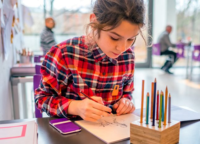 Girl drawing with pencils at a table