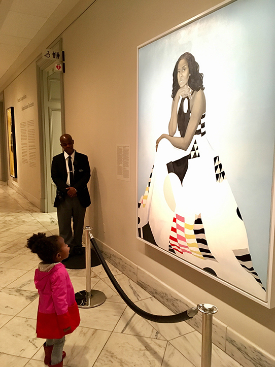 A young girl looks up at a portrait of First Lady Michelle Obama