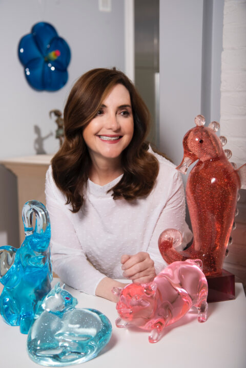 Smiling woman surrounded by lucite sculptures of animals in bright colors
