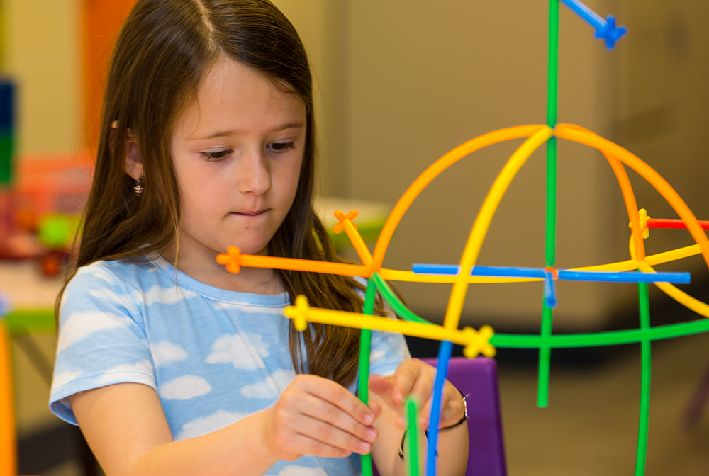 Girl building a structure from colorful sticks.