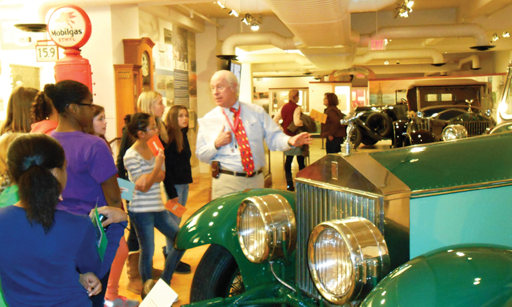 Museum guide with students in front of a vintage car