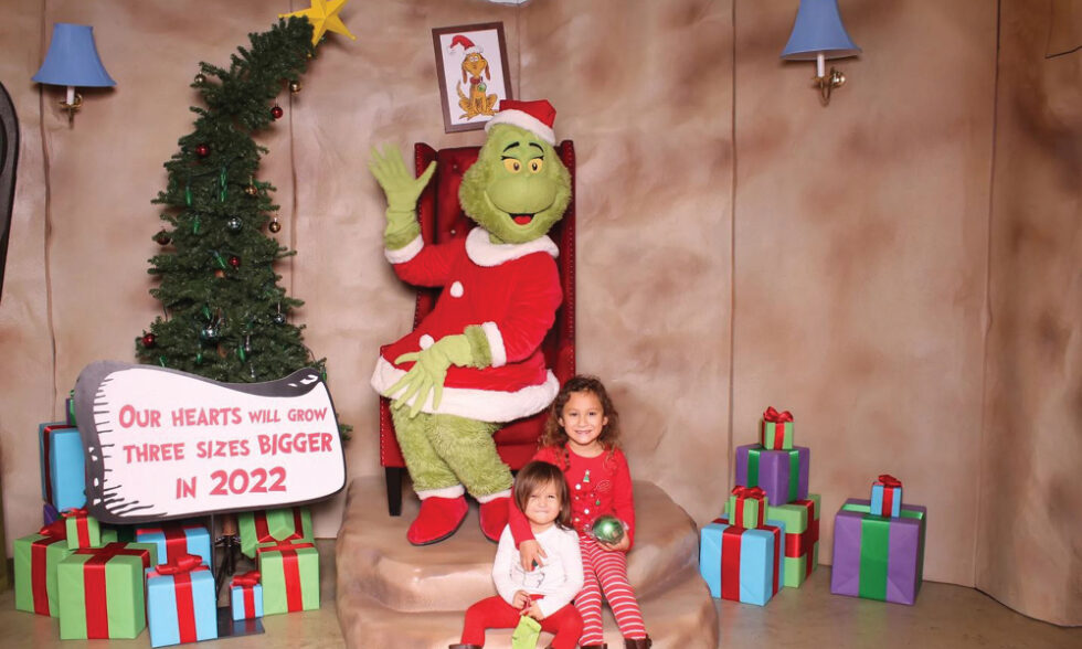 Two children pose with the Grinch costumed character dressed as Santa