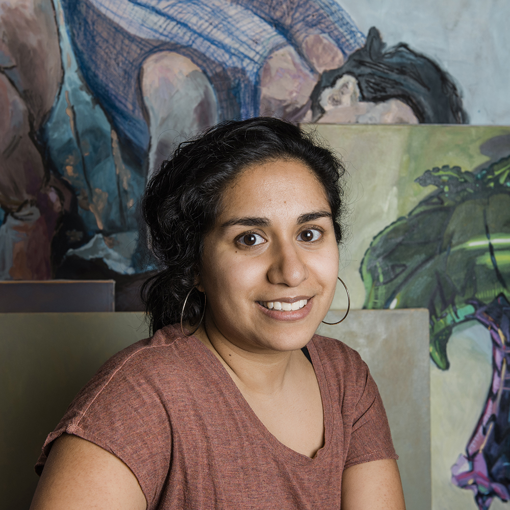 Photo portrait of a woman with dark hair pulled back in a low bun with artwork behind her