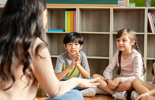 Seated children listening to a woman speak