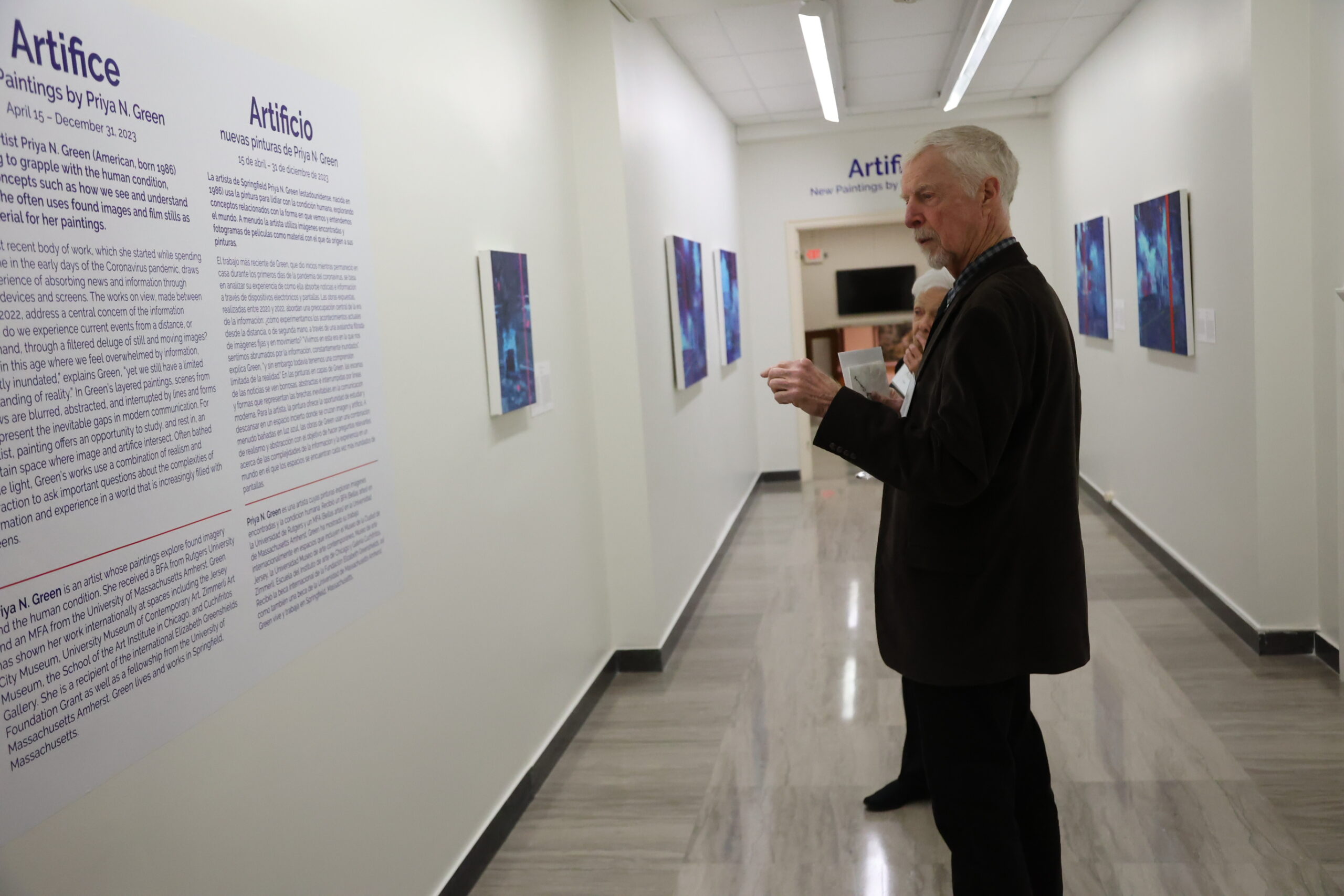 Person examining the "Artifice" art exhibition with someone else hidden behind them