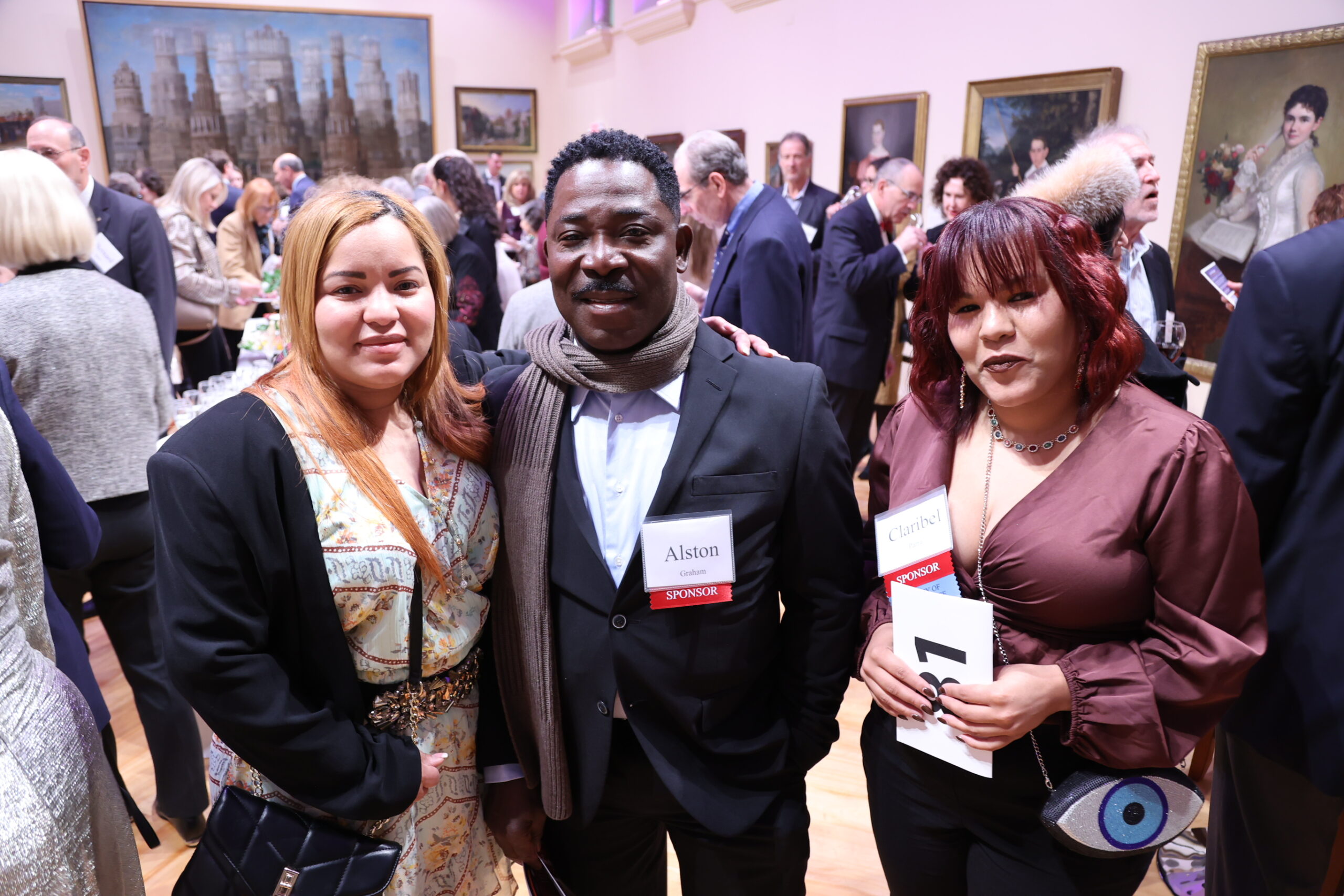 Three people posing for the camera amidst a crowd of people in Black Court hall