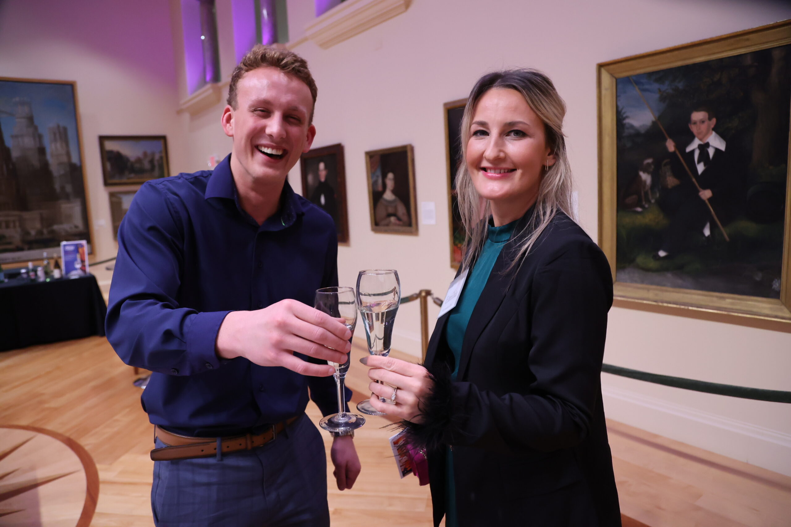 Two people smiling and making a cheers motion with their champagne glasses in the Blake Court hall