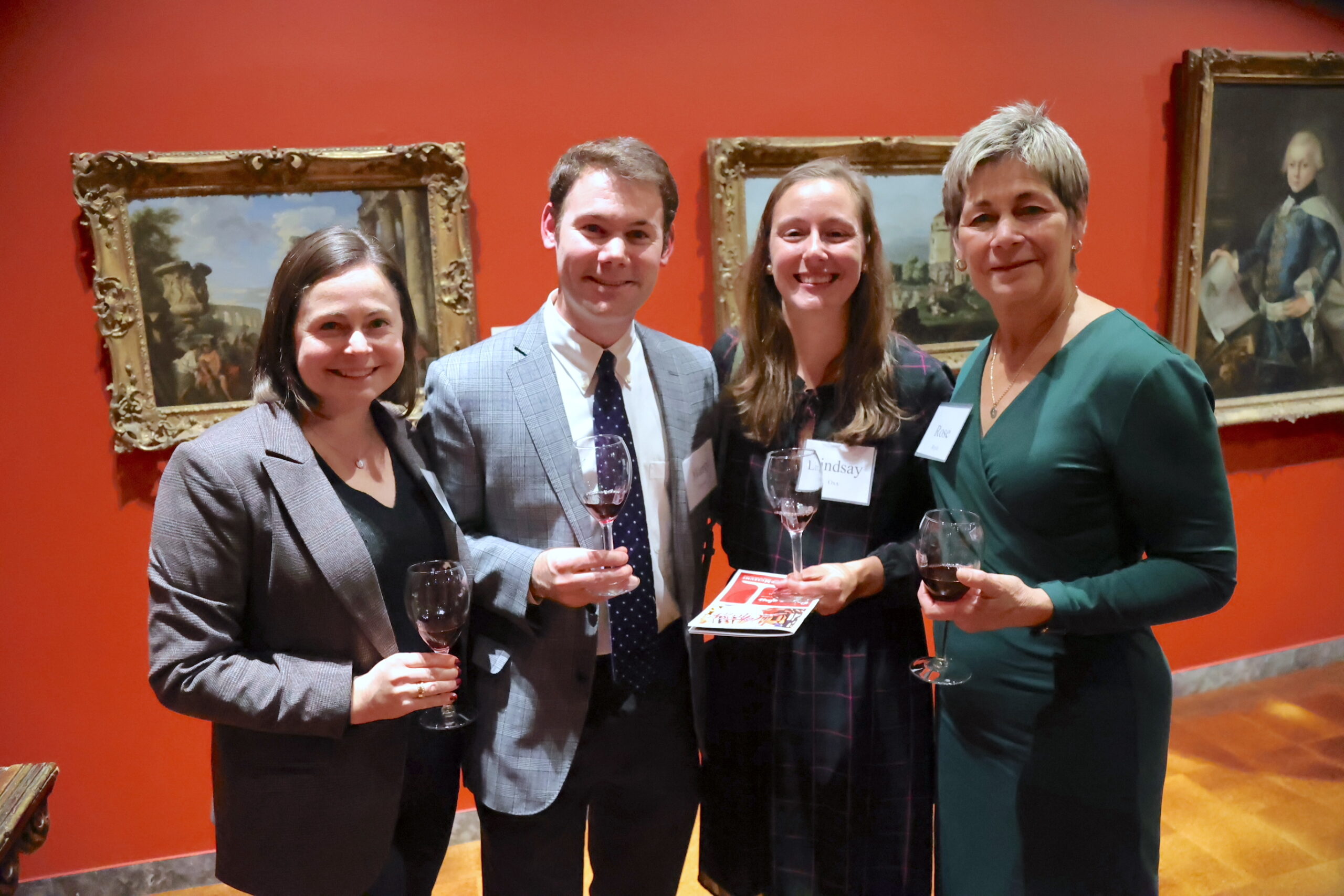 Four people holding wine glasses while standing in an exhibit hall and smiling for the camera