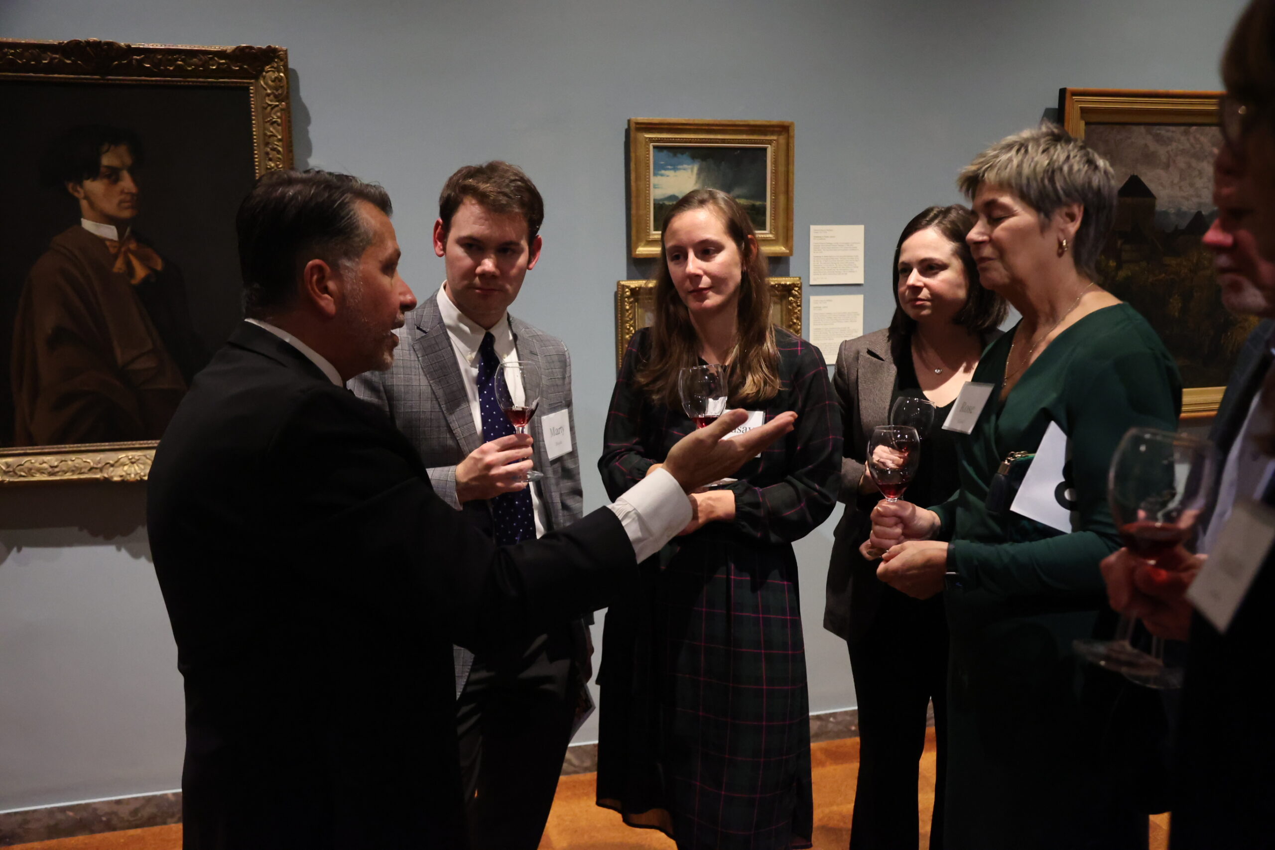 Wine Sommelier Anthony Giglio talking closely with four people, two additional people are peeking in the right side of the frame