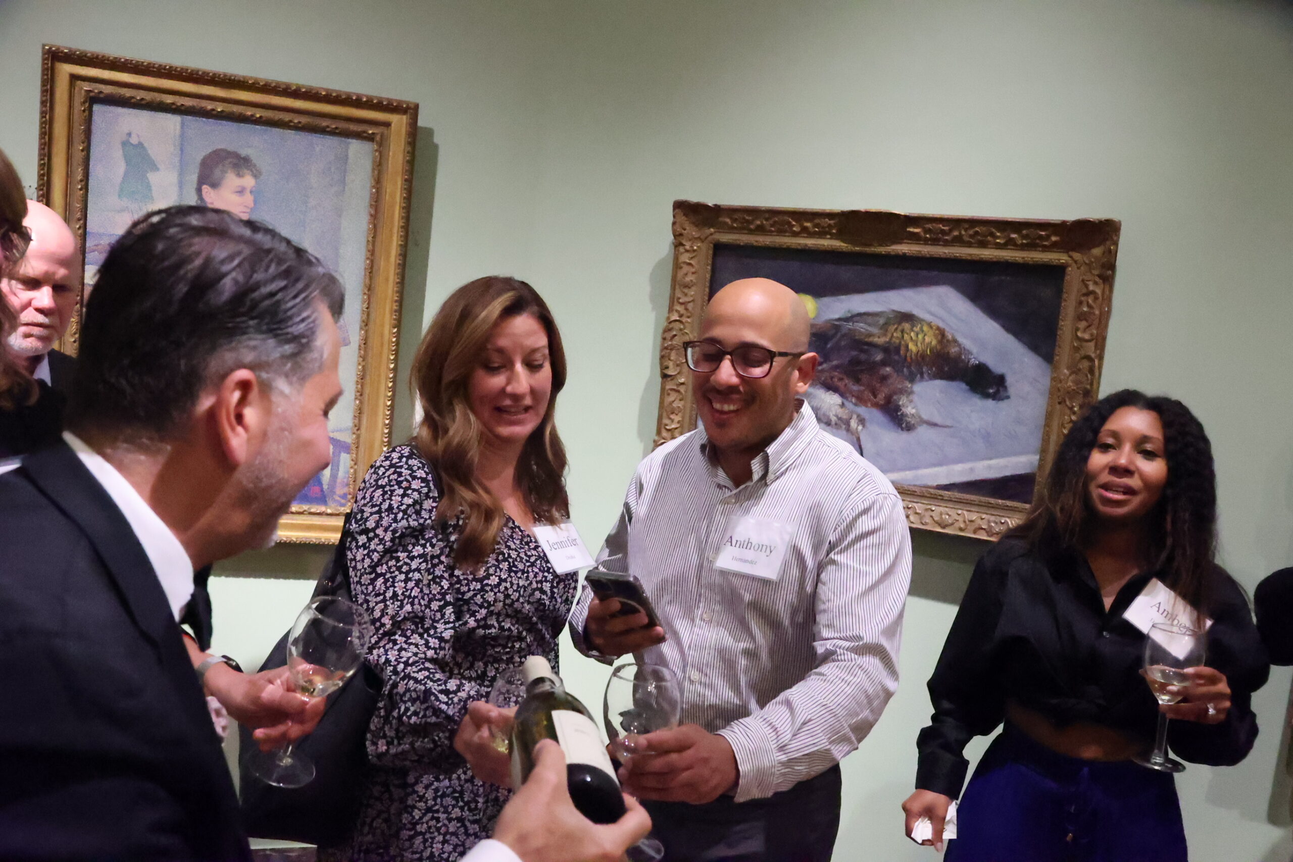 Wine Sommelier Anthony Giglio surrounded by six people, pouring wine in the glass of two of the people present