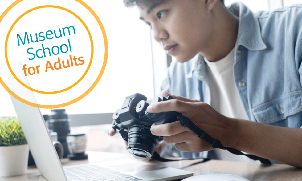 Man seated at a laptop, holding a camera