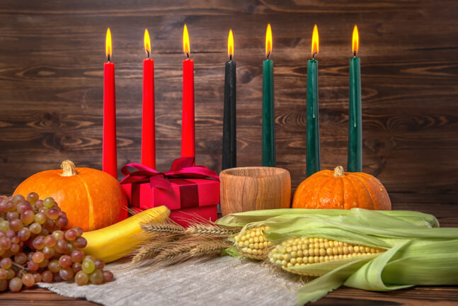 Kwanzaa festival concept with seven candles red, black and green, gift box, pumpkins, ears of wheat, grapes, corns, banana, bowl and fruits on wooden background, close up