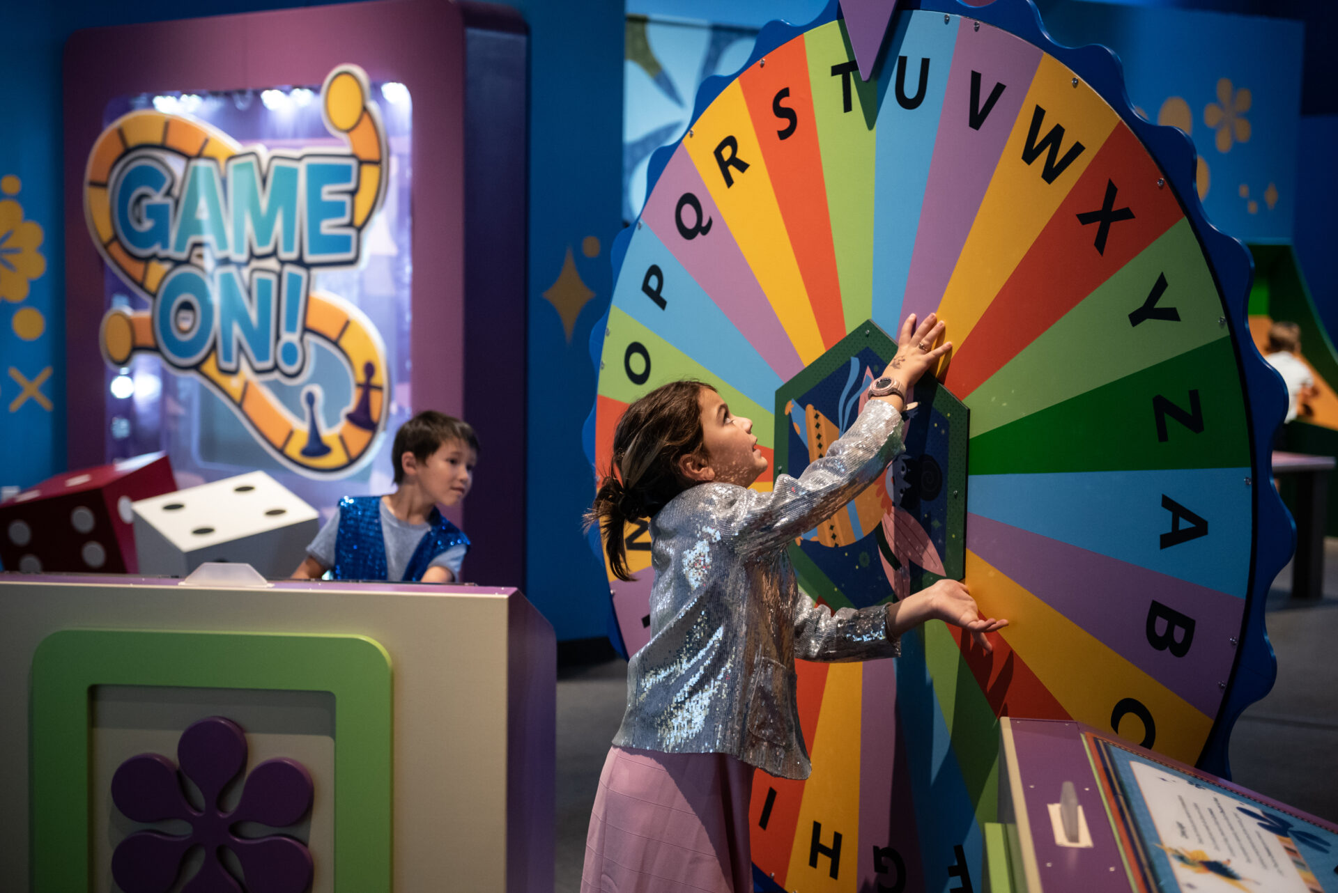 Kids playing on a colorful amusement arcade game with a large spinning wheel featuring alphabet letters in a vibrant indoor setting